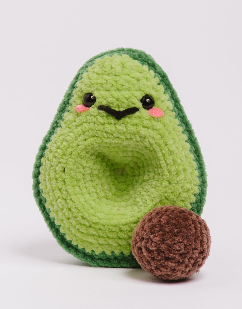 a crocheted avocado half with its stone next to it on an off-white background